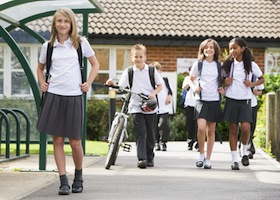 Estudiantes saliendo de la escuela uno con una bicicleta.