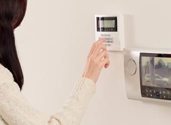 Woman Using Home Security Monitoring System To View Outside